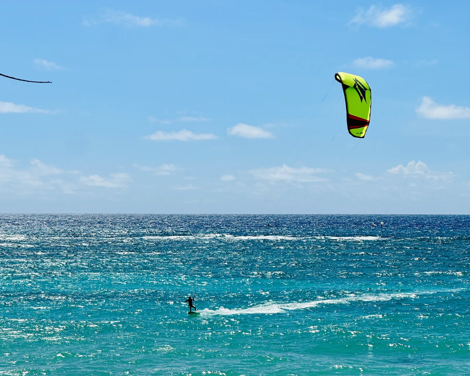 A kitesurfer riding under a green kite on the turquoise sea