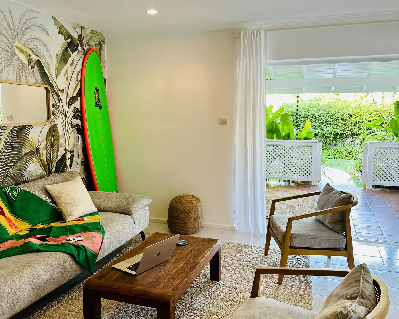 The living room with a surfboard on the wall, open to the porch and garden