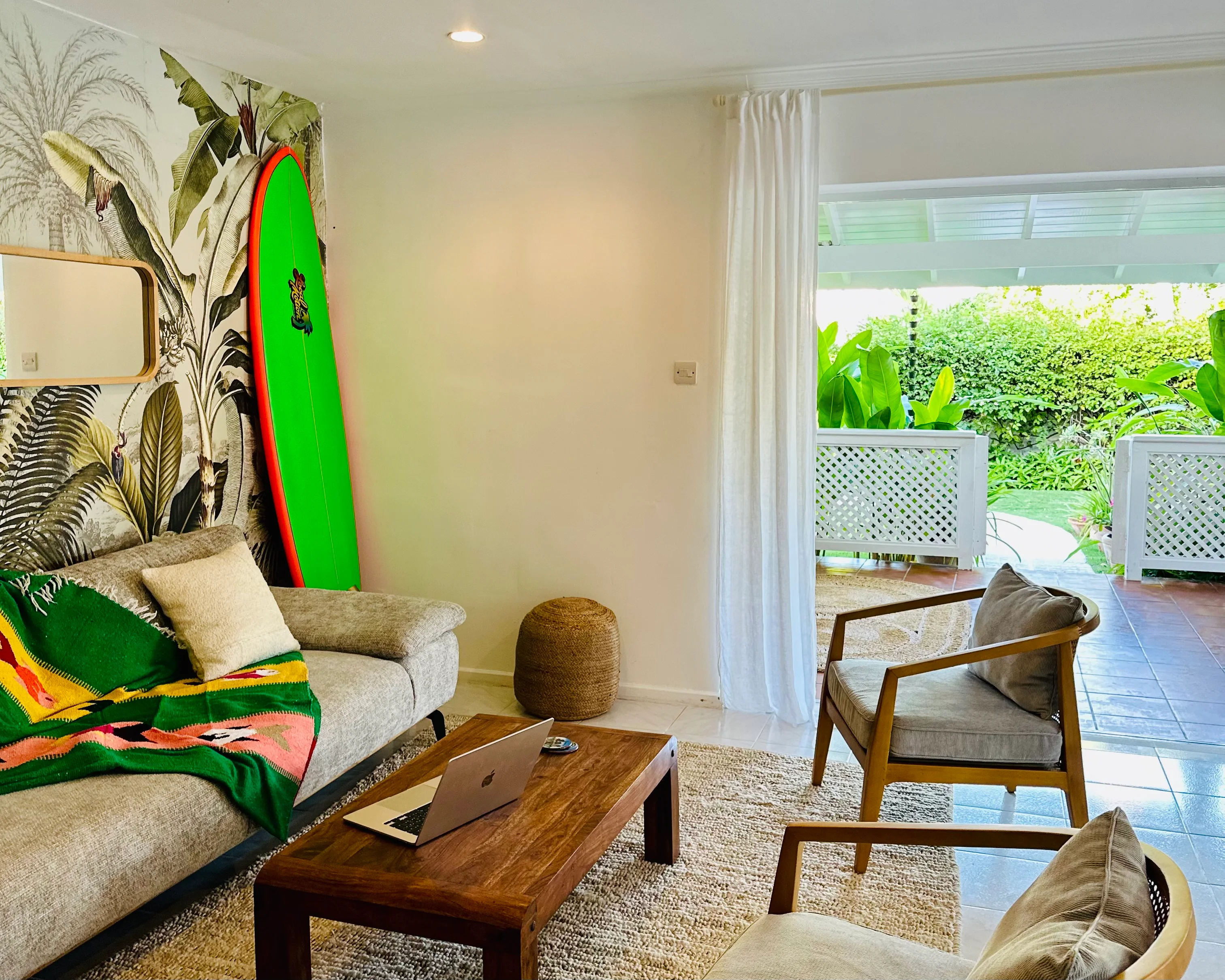 The living room with tropical wallpaper, a green surfboard and a rattan chair