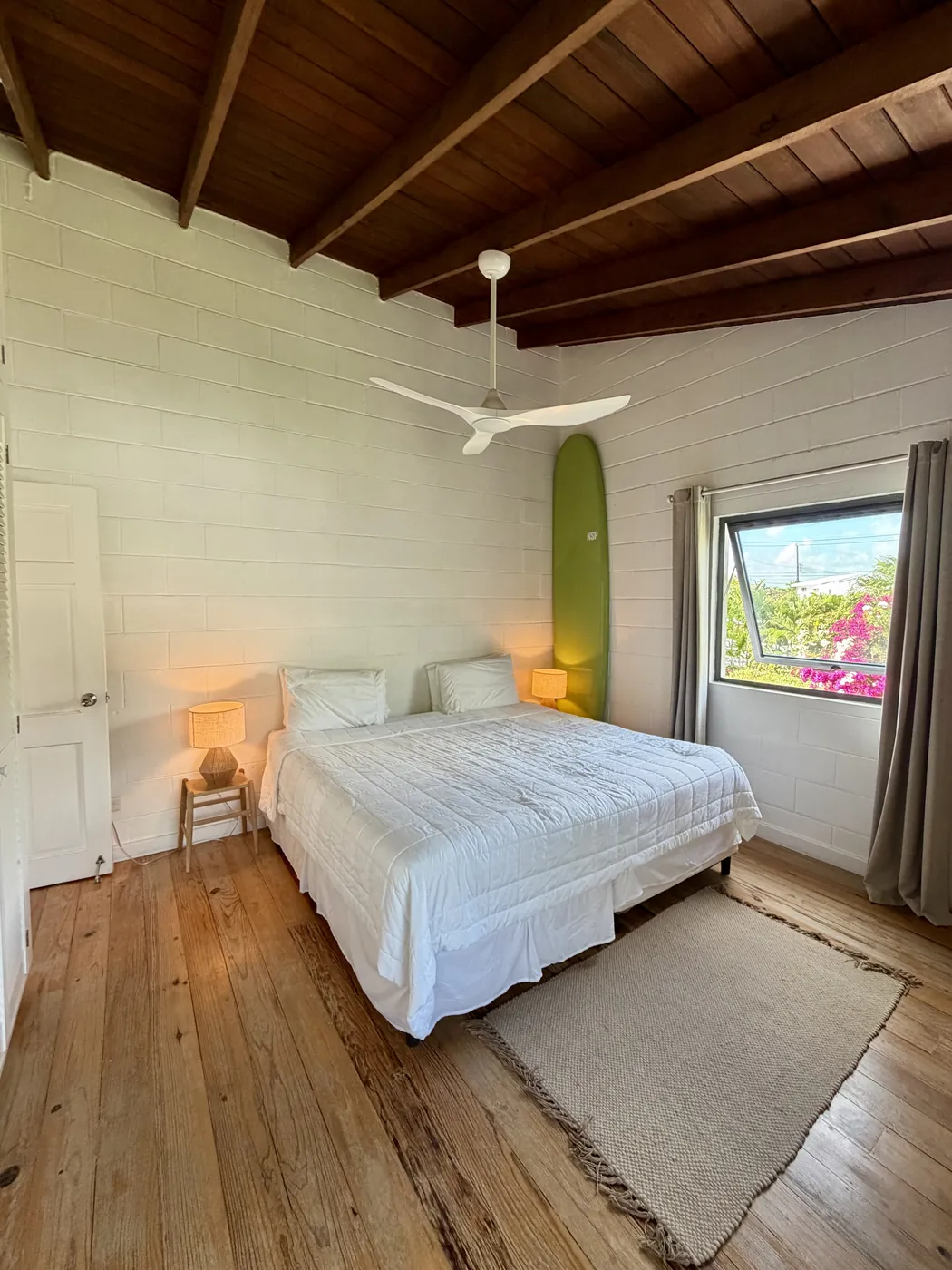 The master bedroom with a rattan headboard, a green surfboard and a wooden ceiling