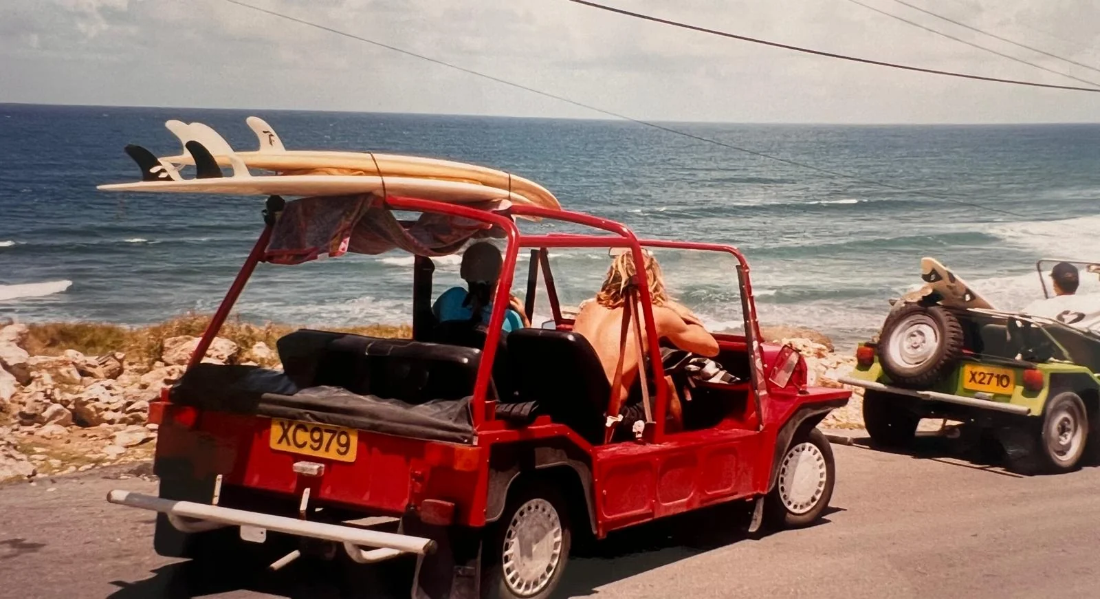 An old photo: two beach jeeps with surfboards on the roof, parked above the sea on the east coast
