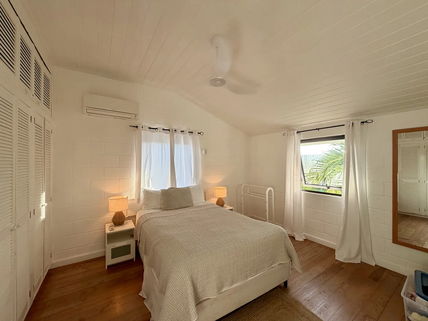 The white bedroom with a queen bed, white curtains and a wooden floor