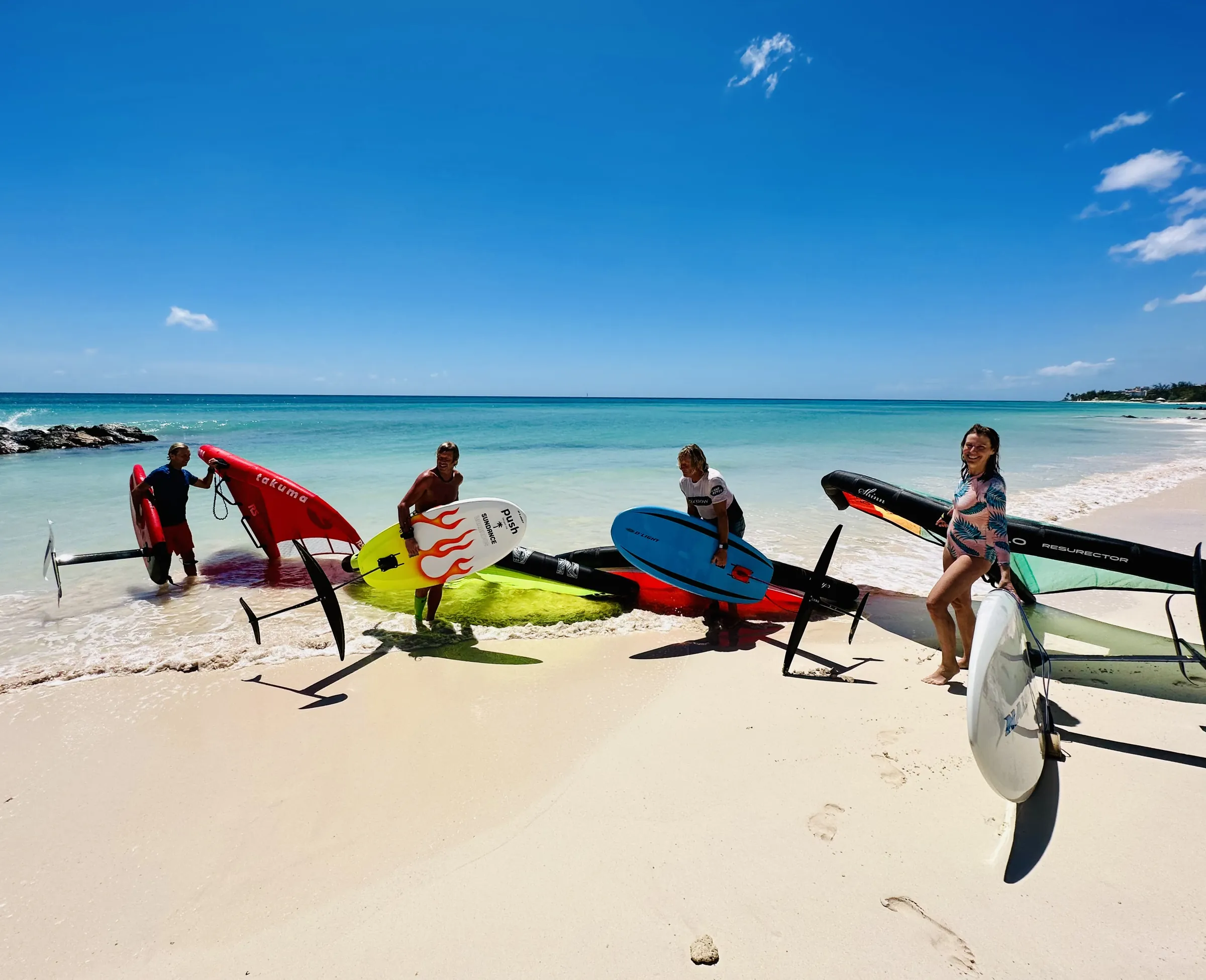 Wingfoilers and kiters with their gear on a white sand beach
